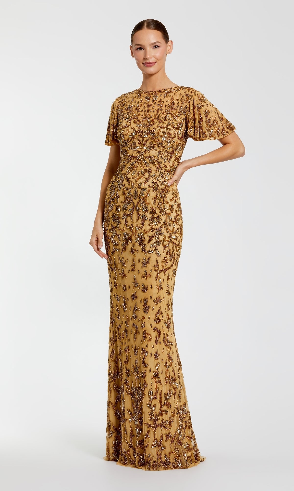 Woman wearing a gold evening gown with floral sequin embellishments in front of a white background